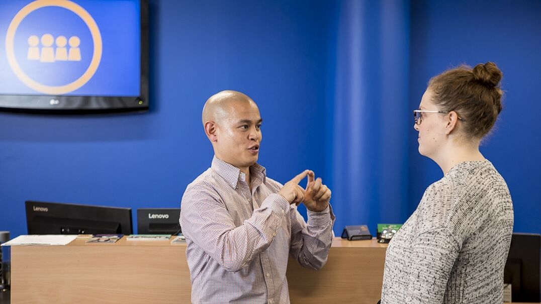 Two people at a reception desk using sign language