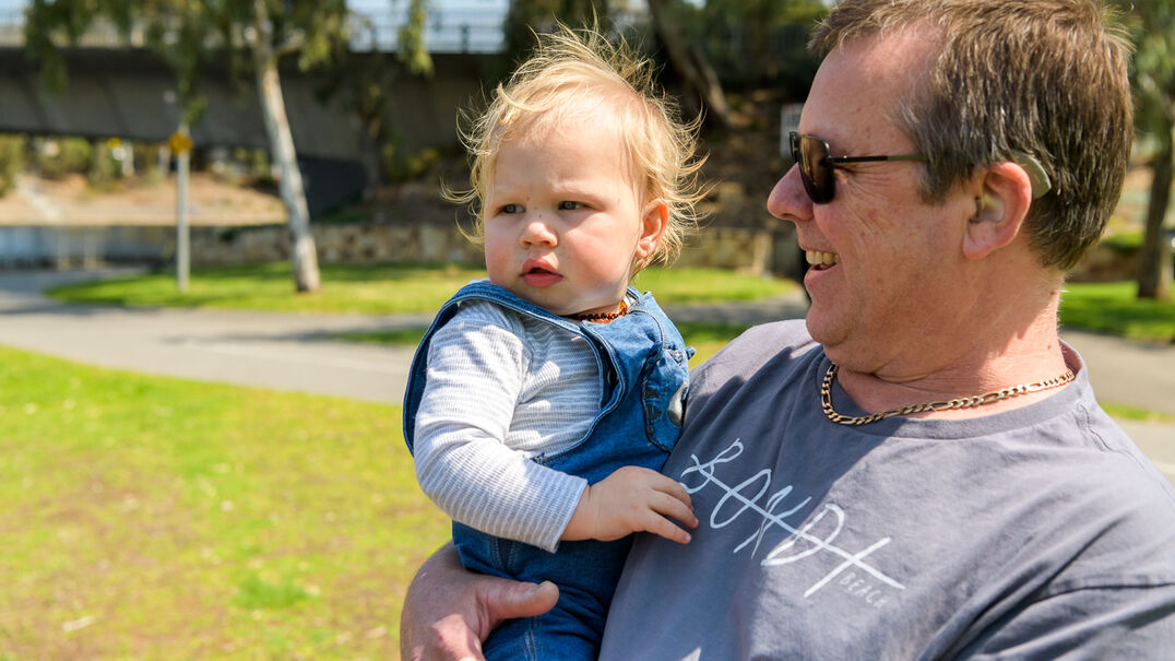 A deaf man holding a baby in a sunny park